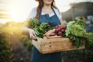 Mulher carregando bandeja com alimentos naturais & orgânicos, entre eles, cenoura, rabanete e alface