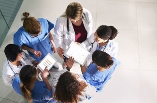 Grupo de 7 médicos reunidos, 2 deles estão com um tablet em suas mãos